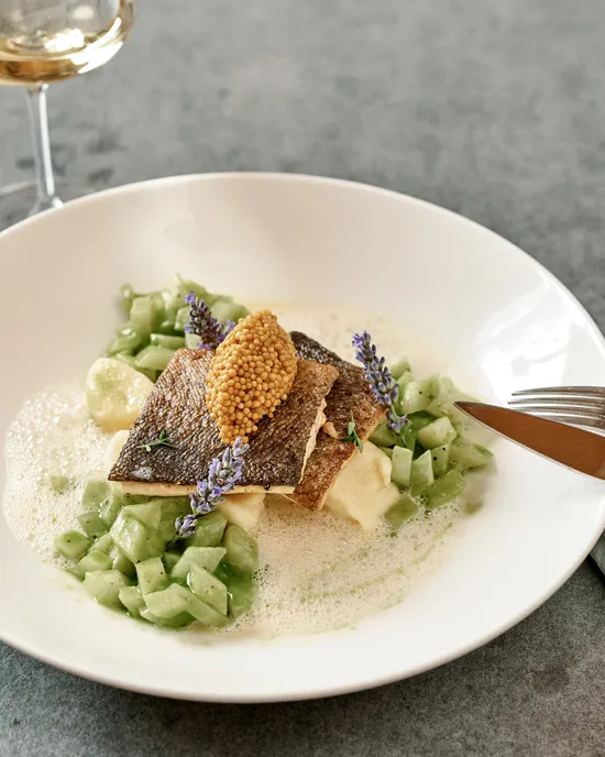 Gourmet-Fischfilet mit Senfkörnern, Gurkenwürfeln und essbaren Blüten auf cremiger Schaumsauce